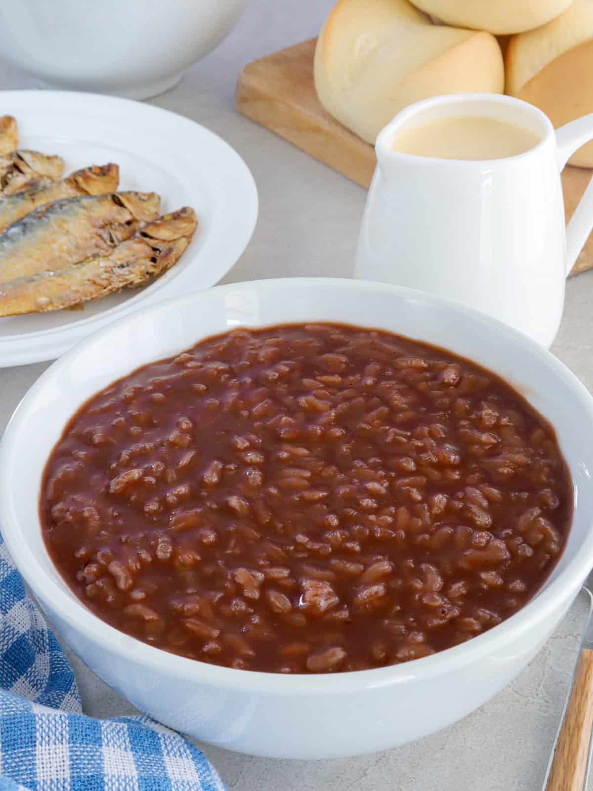 champorado in a white bowl with fried tuyo and evaporated milk in the background.