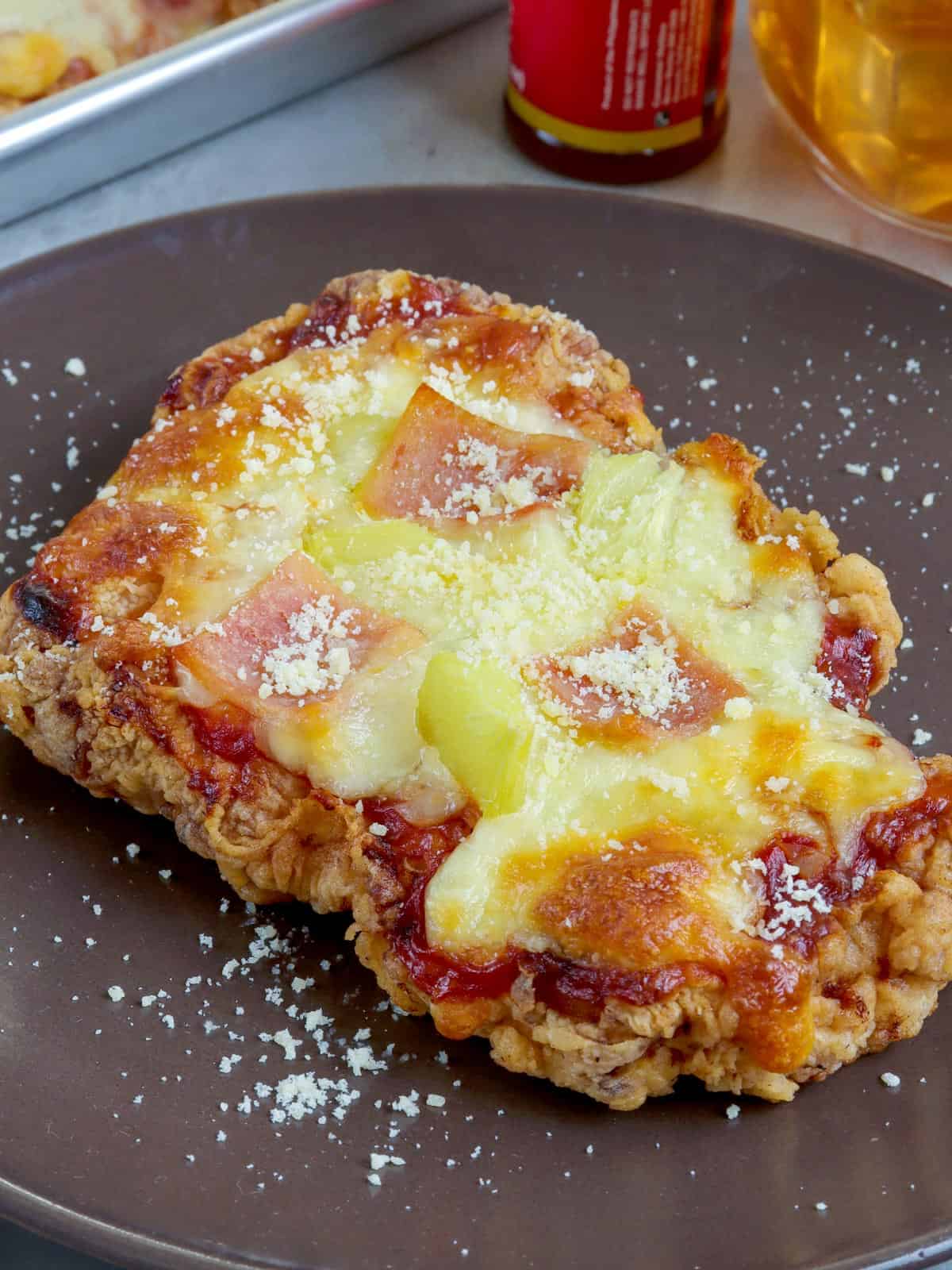 crispy breaded chicken breast baked with cheese, ham, and pineapple toppings on a brown plate.