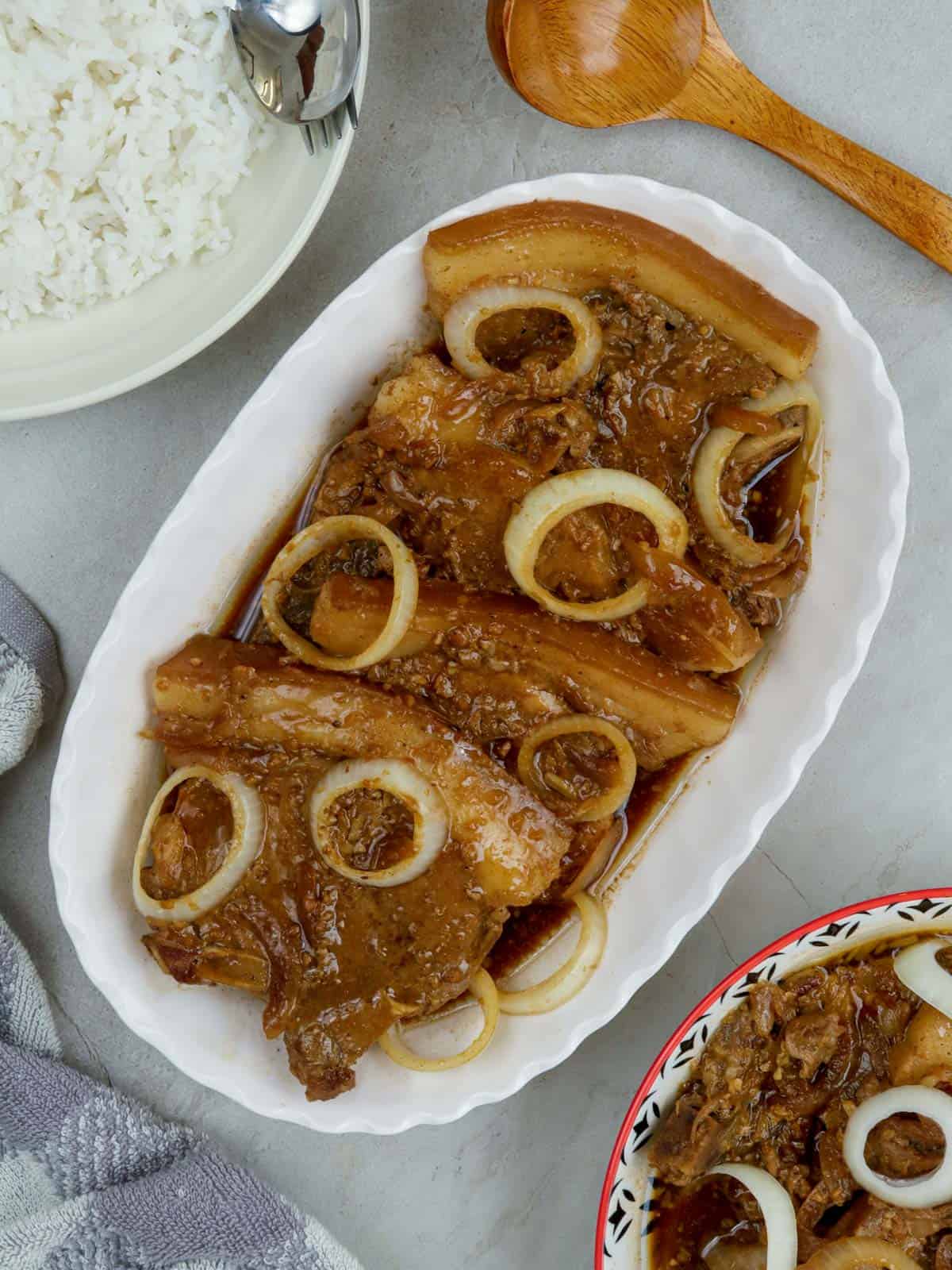 pork bistek garnished with onion rings on a serving platter with a plate of steamed rice on the side