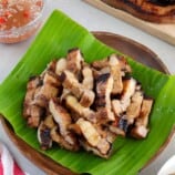 sliced Inihaw na Liempo on a banana leaf-lined wooden plate with a bowl of vinegar dipping sauce in the background.